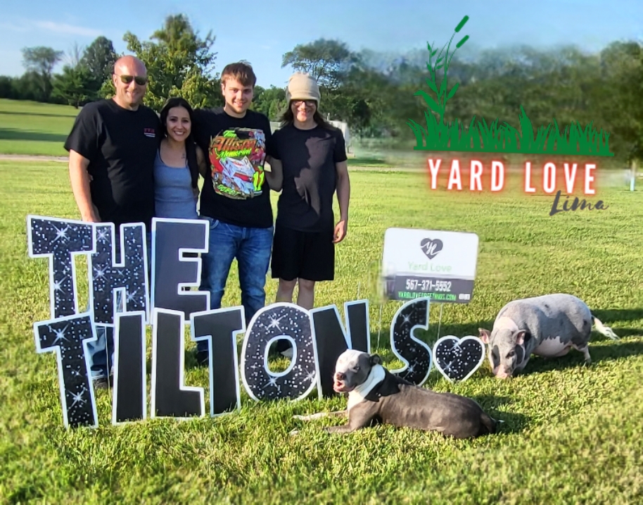 Family with pet dog and pig with yard signs saying The Tilton's
