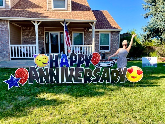 Woman waving next to Happy Anniversary yard signs