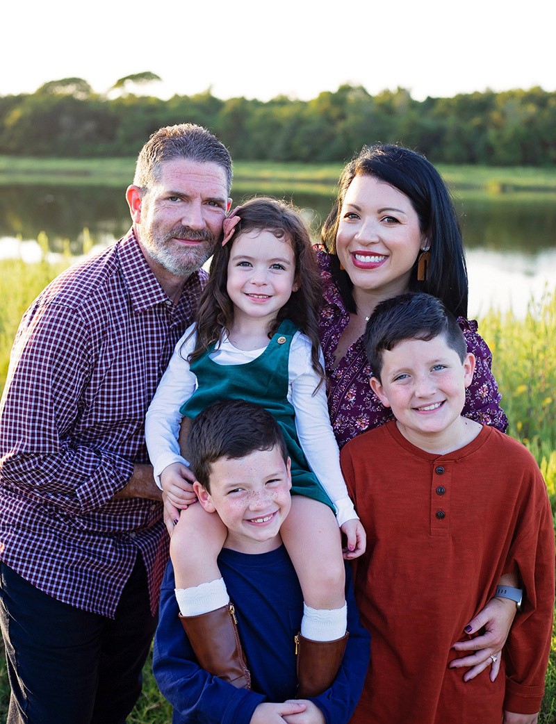 Geneva & Marcus Gandy and their 3 children - 2 boys and a girl. In front of a beautiful lake surrounded by green trees and grasses