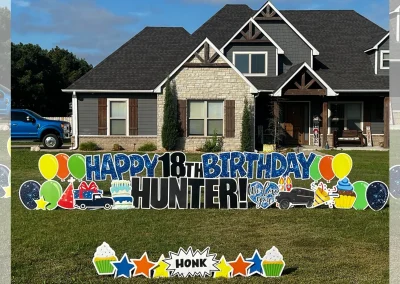 YL Broken Arrow sign - "Happy 18th Birthday, Hunter!" Glittery blue and black letters surrounded by multicolored balloons, cars and cake